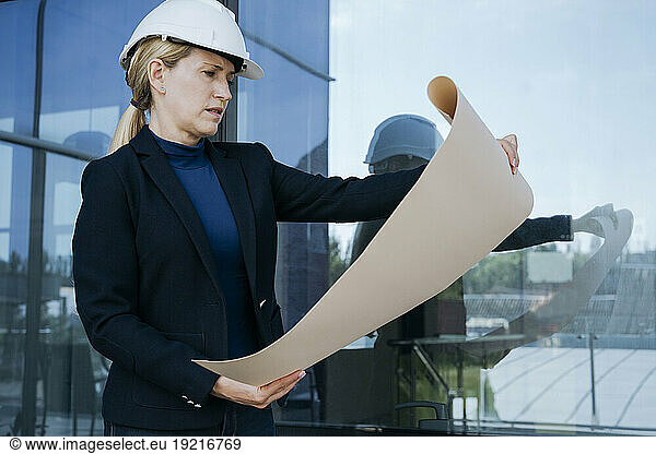 Female architect examining blueprint near office building