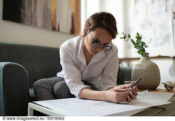 Female architect with smartphone reading draft