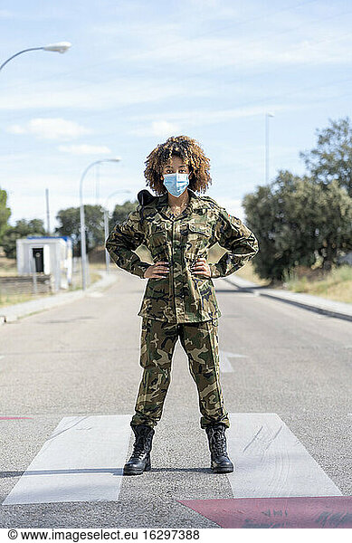 Female army soldier wearing protective face mask with hands on hip standing on street