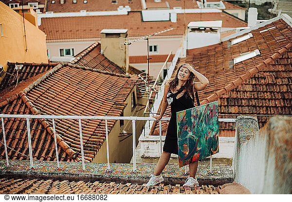 Female artist holding canvas while standing on tiled roof with view