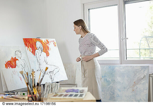 Female artist looking at canvas in home studio