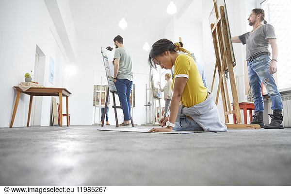 Female artist sketching on floor in art class studio