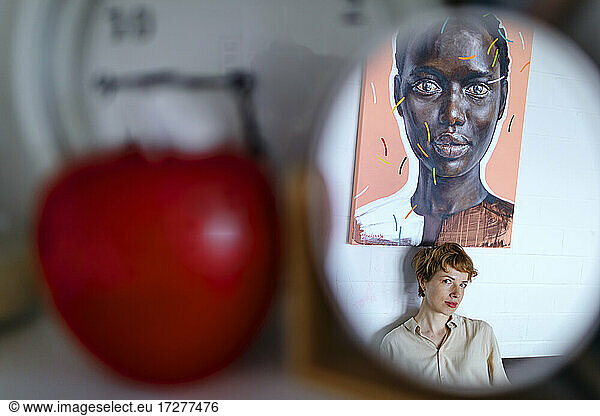Female artist standing below painting reflecting on mirror in studio