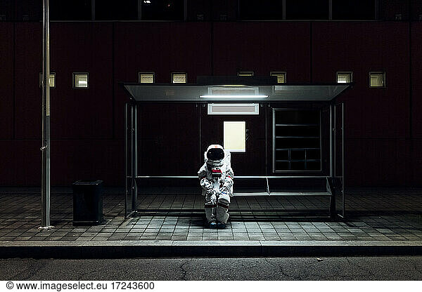 Female astronaut sitting at bus stop during night