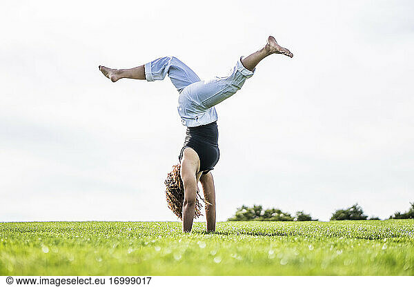 Female athlete exercising cartwheel on grass in park against clear sky