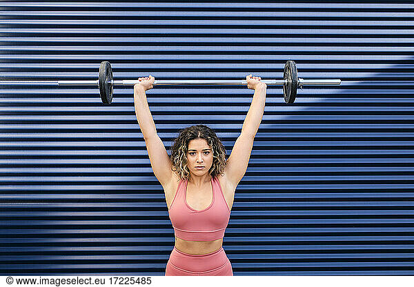 Female athlete lifting barbell in front of blue corrugated wall