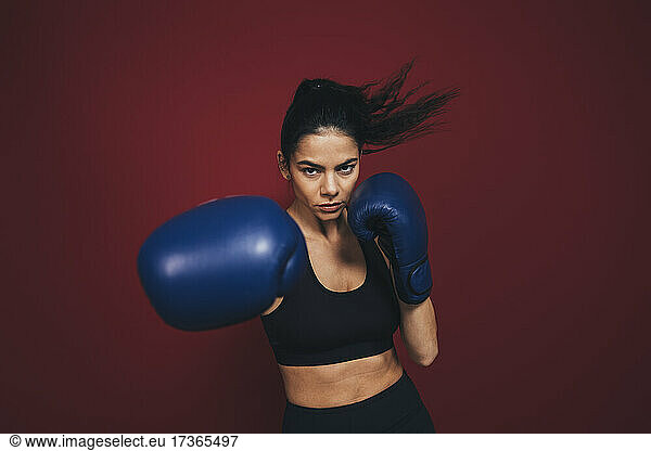 Female athlete practicing boxing in front of maroon background