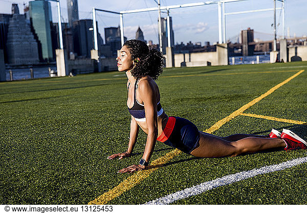 Female athlete practicing cobra pose on grassy field