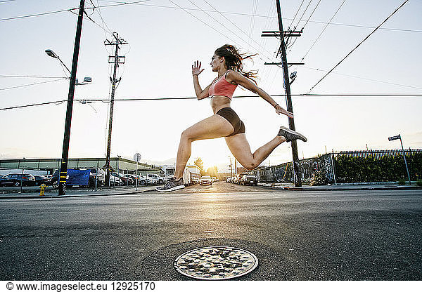 Female athlete running along street at dusk.