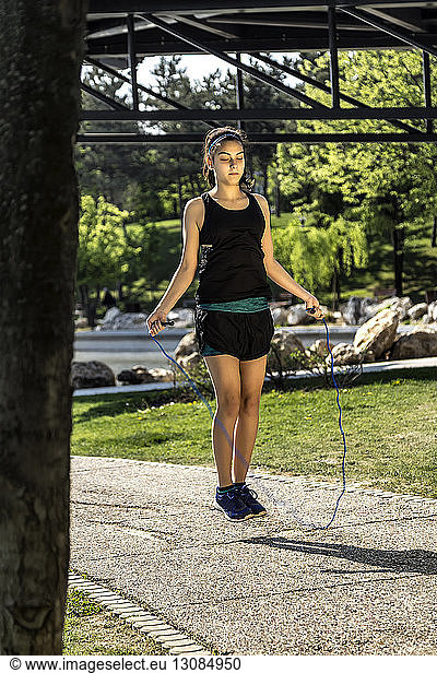 Female athlete skipping with jump rope on footpath at park