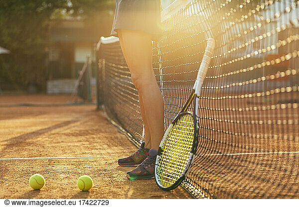Female athlete standing by tennis racket and ball at sports court during sunny day