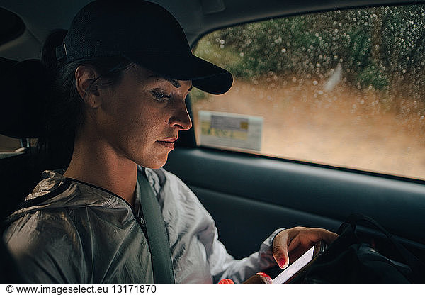 Female athlete using mobile phone while traveling in car during rainy season