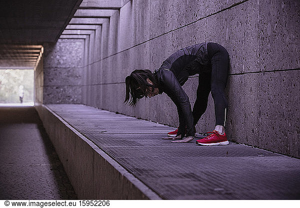 Female athlete warming up before running in pedestrian underpass