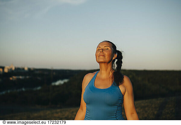 Female athlete with eyes closed against sky during sunset