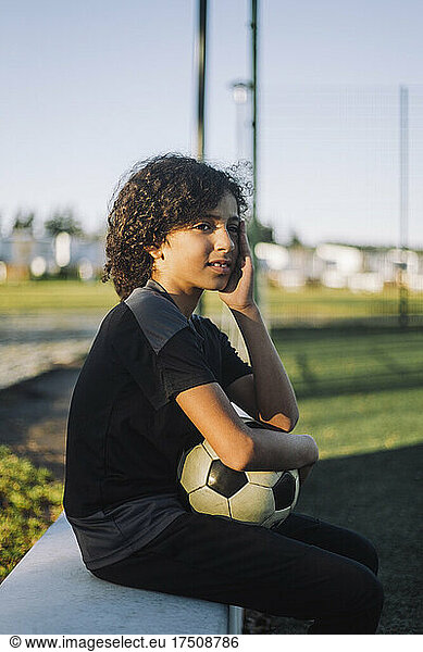Female athlete with soccer ball sitting on retaining wall