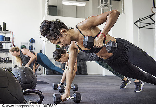 Female athletes doing push-ups using dumbbells in crossfit gym
