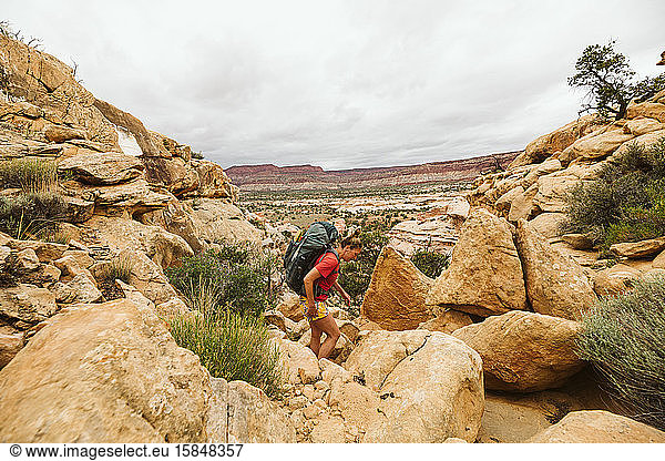female backpacker hikes over rocky rugged terrain in utah desert