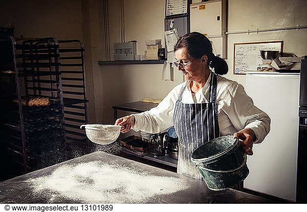 Female baker sprinkling flour on table at bakery