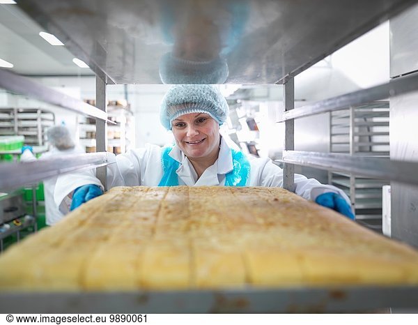 Female baker with tray of cakes in cake factory