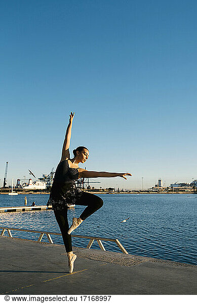 Female ballet dancer practicing on jetty at marina against clear sky