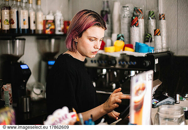 Female barista working at checkout counter on a tablet in coffee shop