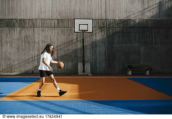 Female basketball player dribbling ball at sports court