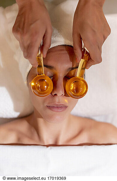 Female beautician holding glass globes on customer's face at health spa
