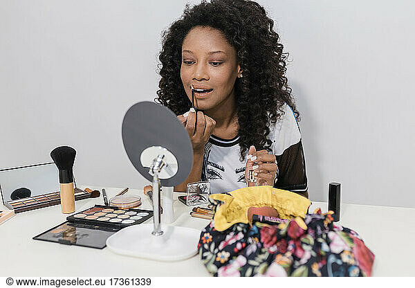 Female beauty expert applying lip gloss while looking at mirror