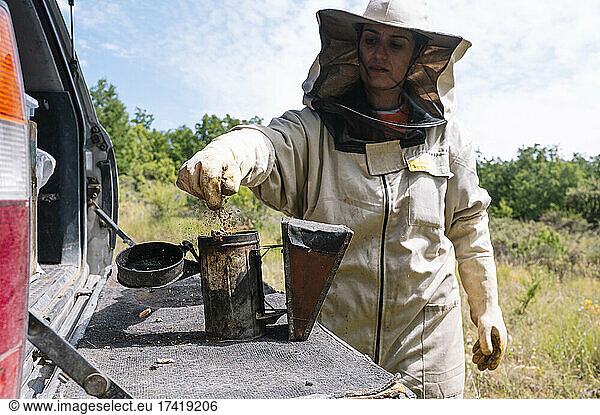 Female beekeeper using bee smoker at farm