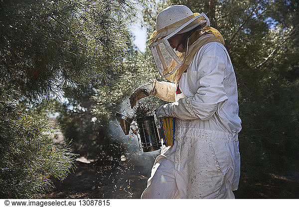 Female beekeeper using beehive smoker while working