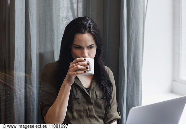 Female blogger drinking coffee while working in creative office