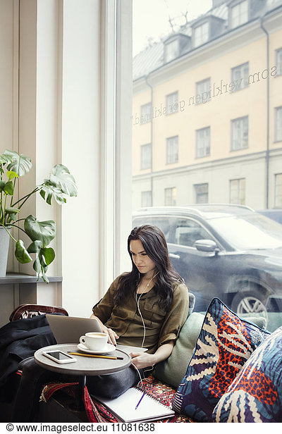 Female blogger working while sitting on sofa by window in office