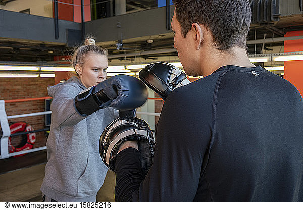 Female boxer sparring with her coach in gym