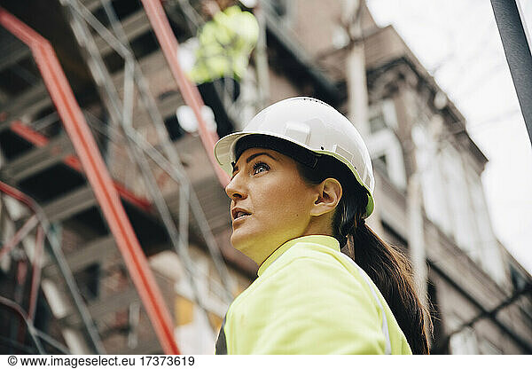 Female building contractor in hardhat looking away at construction site