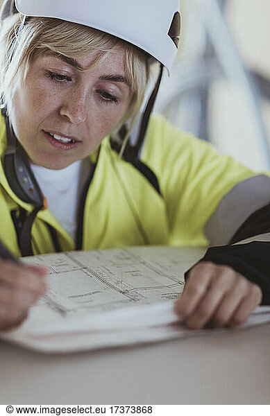 Female building contractor writing while analyzing floor plan at construction site