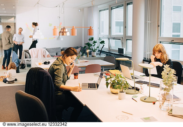 Female business colleagues working at illuminated desk in creative office