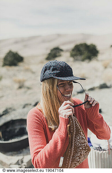 female camper in brimmed hat and sweater smiles and puts on sunglasses