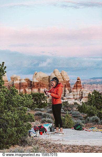 female camper in orange puffy jacket takes a swig of whiskey in desert
