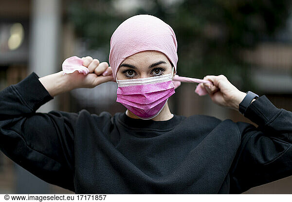 Female cancer patient in bandana wearing pink protective face mask during COVID-19