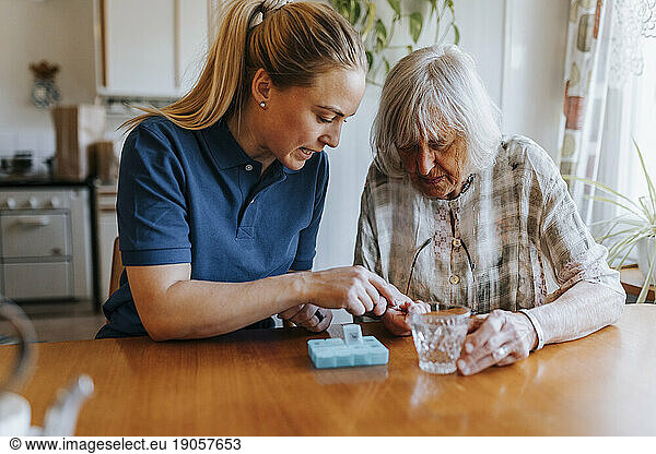 Female caregiver assisting senior woman while taking medicines at home