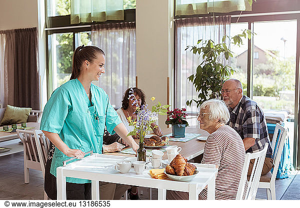Female caregiver serving meal to senior people in nursing home