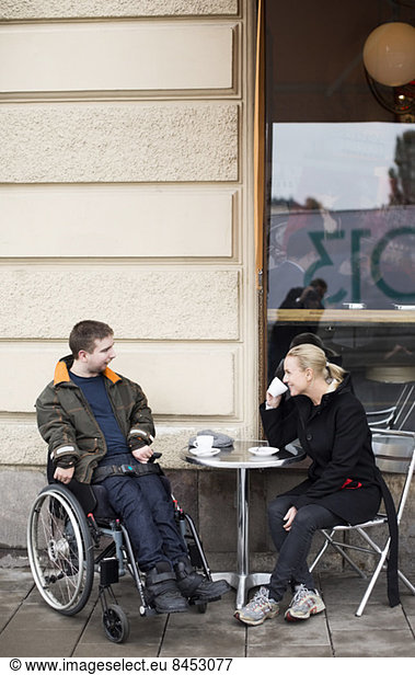 Female caretaker and disabled man having coffee at sidewalk cafe