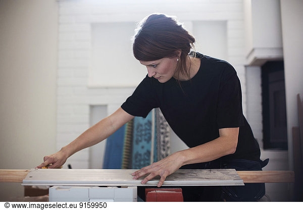 Female carpenter measuring wooden plank