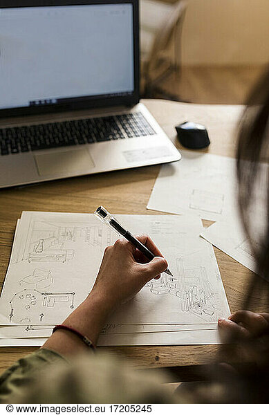Female carpenter with laptop making design on paper at desk in industry