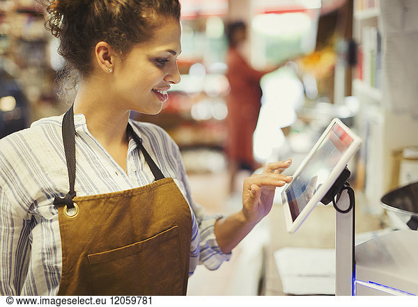 Female cashier using touch screen cash register in grocery store