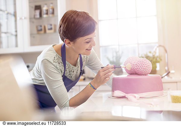 Female caterer finishing pink wedding cake in kitchen