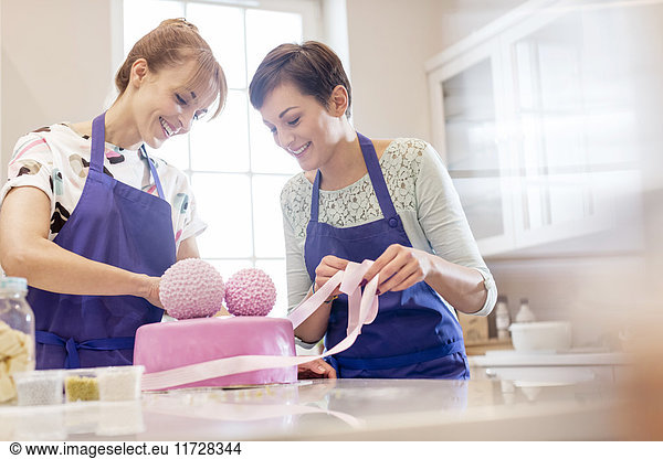 Female caterers finishing pink wedding cake in kitchen