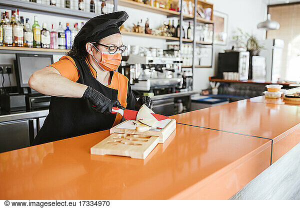 Female chef cutting manchego cheese at counter during pandemic