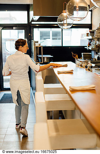 Female chef putting napkins on bar counter in open kitchen restaurant