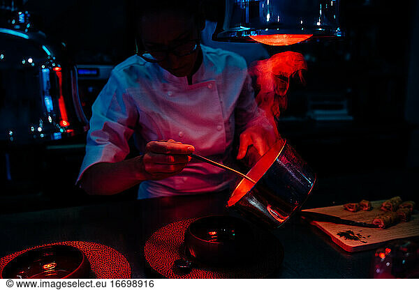 Female chef serving hot meal in restaurant kitchen with heat lamps